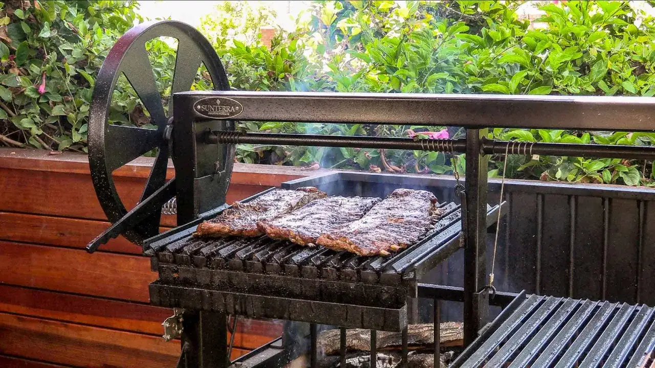Trois belles côtes de porc grillent sur un barbecue extérieur. Une recette de ribs parfaite pour l'été.