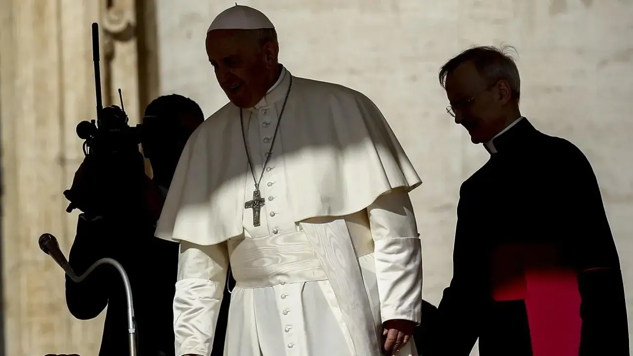 Papst Franziskus, der sich gegen Abtreibung ausspricht, geht mit einem Begleiter. Eine Kamera ist im Vordergrund zu sehen.
