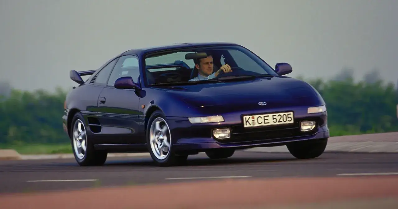 Mężczyzna za kierownicą fioletowego Toyota MR2 SW20, jadącego po drodze.