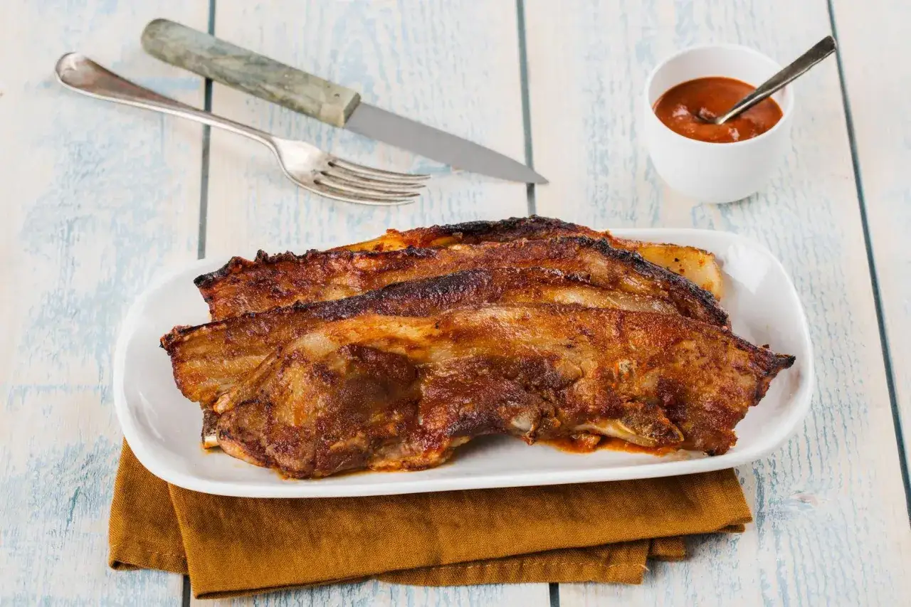 Côtelettes de porc marinées pour un barbecue savoureux, servies avec une sauce barbecue et des couverts.