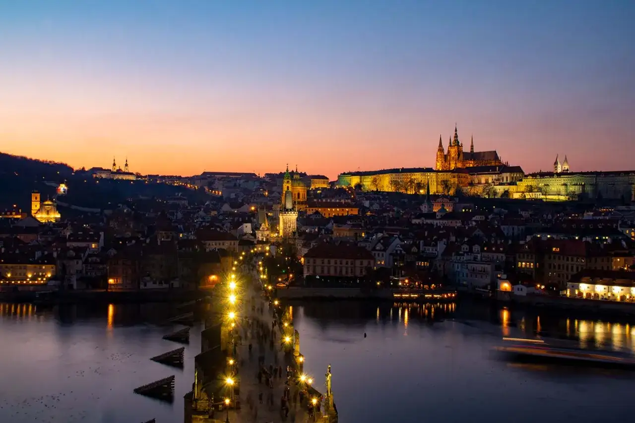 Vue panoramique de Prague au cr&eacute;puscule, avec le ch&acirc;teau illumin&eacute; et le pont Charles anim&eacute;. Une vue magique depuis un rooftop.