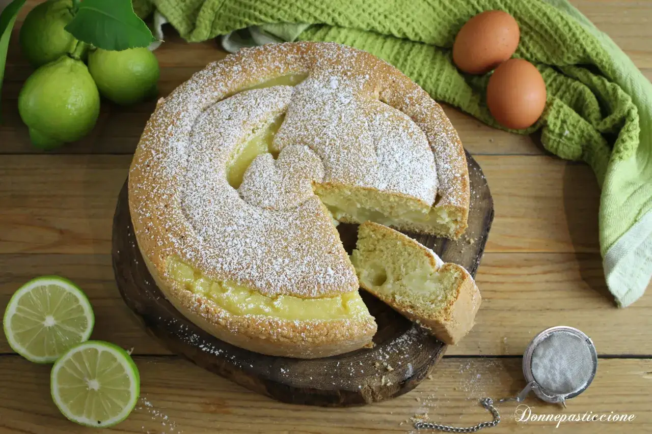 Deliziosa torta all'acqua spolverata di zucchero a velo, con un ripieno cremoso. Accanto, limoni freschi e uova, ingredienti per un dolce leggero e profumato.