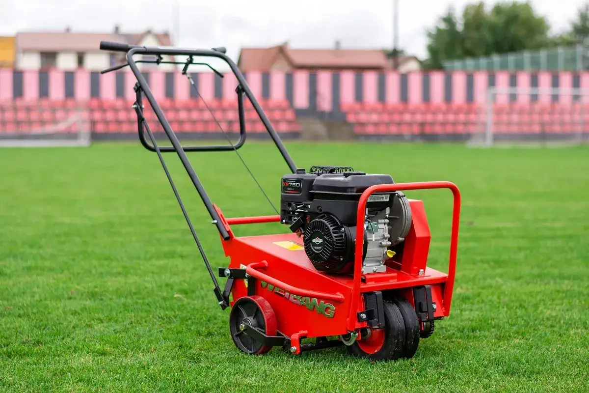 Czerwony aerator spalinowy na zielonej murawie stadionu. Idealne narzędzie, gdy aerować trawnik, by zapewnić mu zdrowy wygląd.