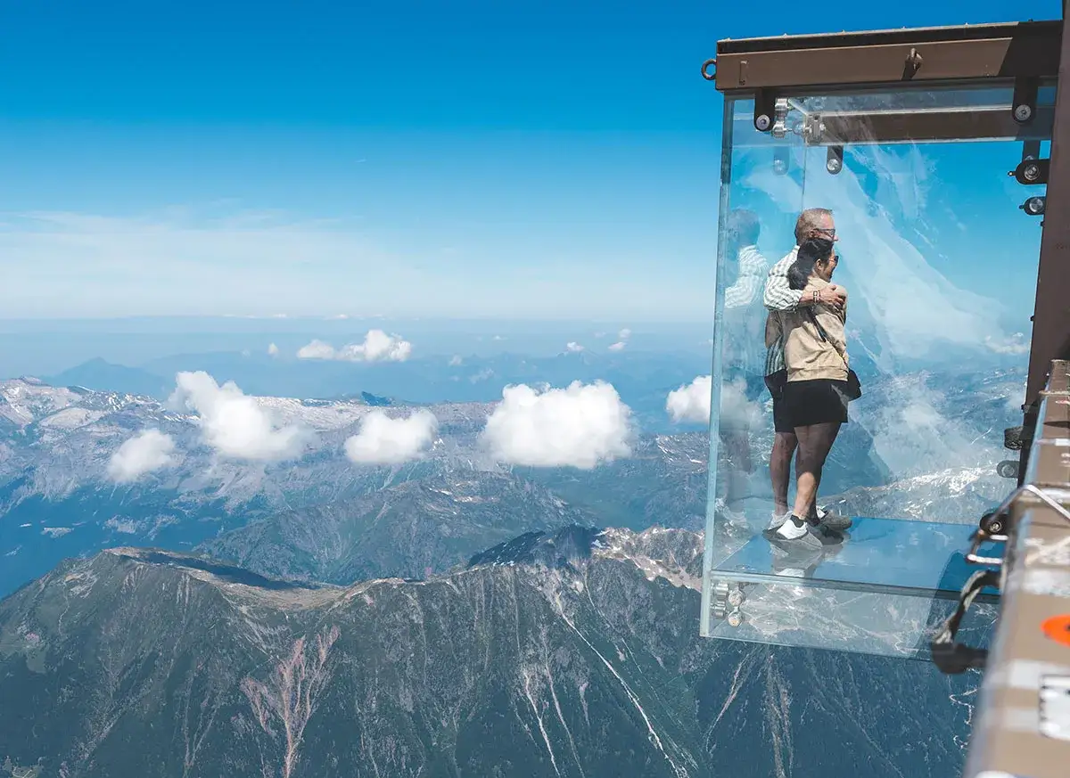 Un couple s'embrasse dans une cabine de verre suspendue au-dessus des montagnes, d&eacute;fiant la peur du vide.