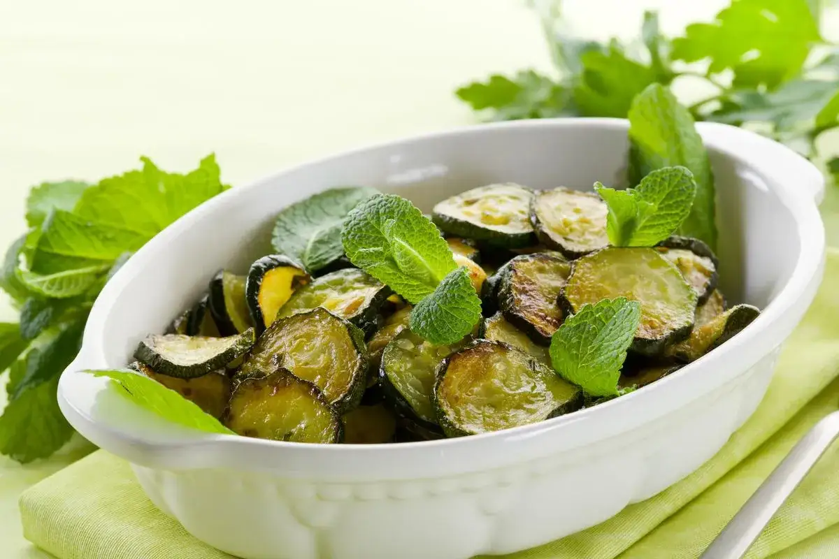 Zucchine alla poverella dorate e profumate, guarnite con foglie di menta fresca in una ciotola bianca.