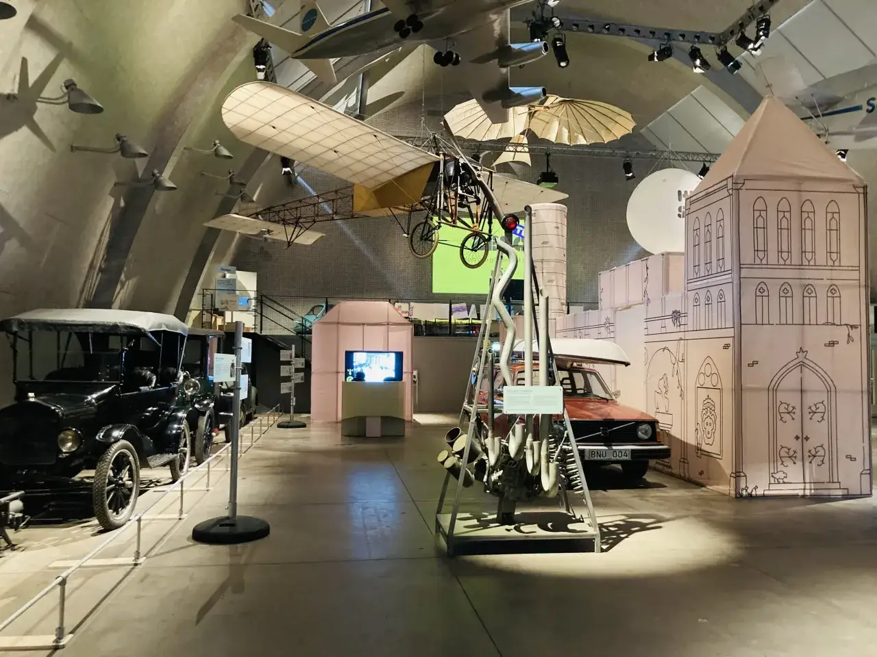 Gamla bilar och flygplan hänger i taket på tekniska museet. En utställning om fordon och flyg.