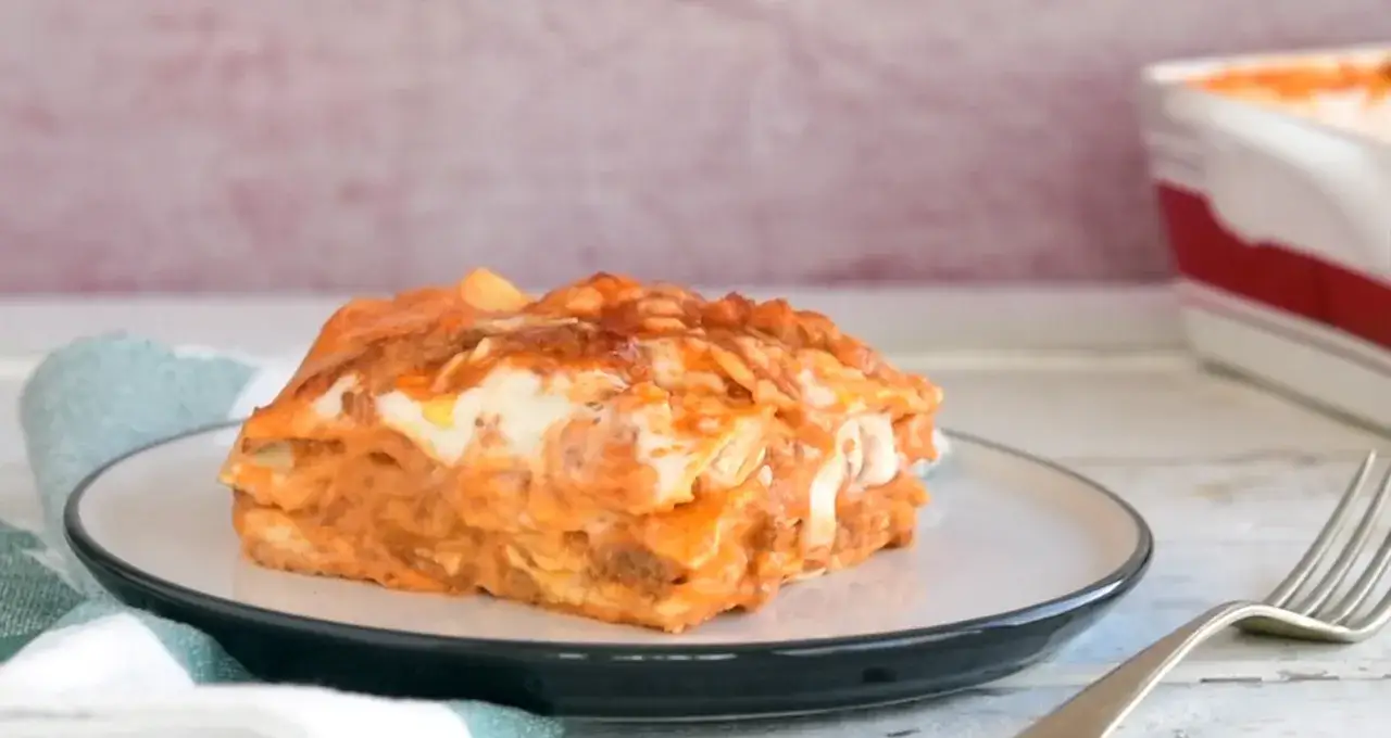 Ein St&uuml;ck Lasagne al Ragu auf einem Teller, mit geschmolzenem K&auml;se und einer Gabel daneben.