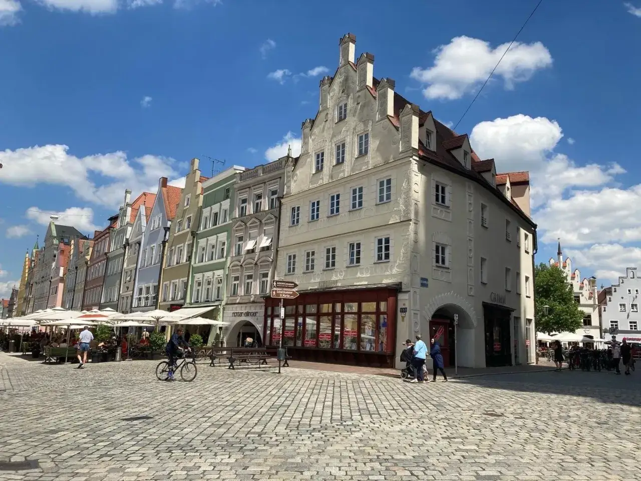Bunte Giebelh&auml;user s&auml;umen den Platz, ein Radfahrer f&auml;hrt vorbei. Hier gibt es viele Landshut Geheimtipps zu entdecken.