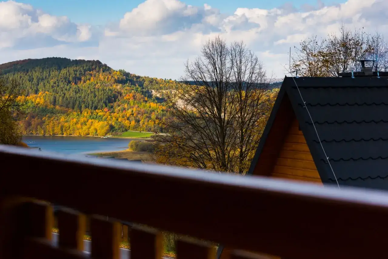 Drewniany olchowiec nad Soliną, otoczony jesiennymi barwami lasów i błękitem nieba.