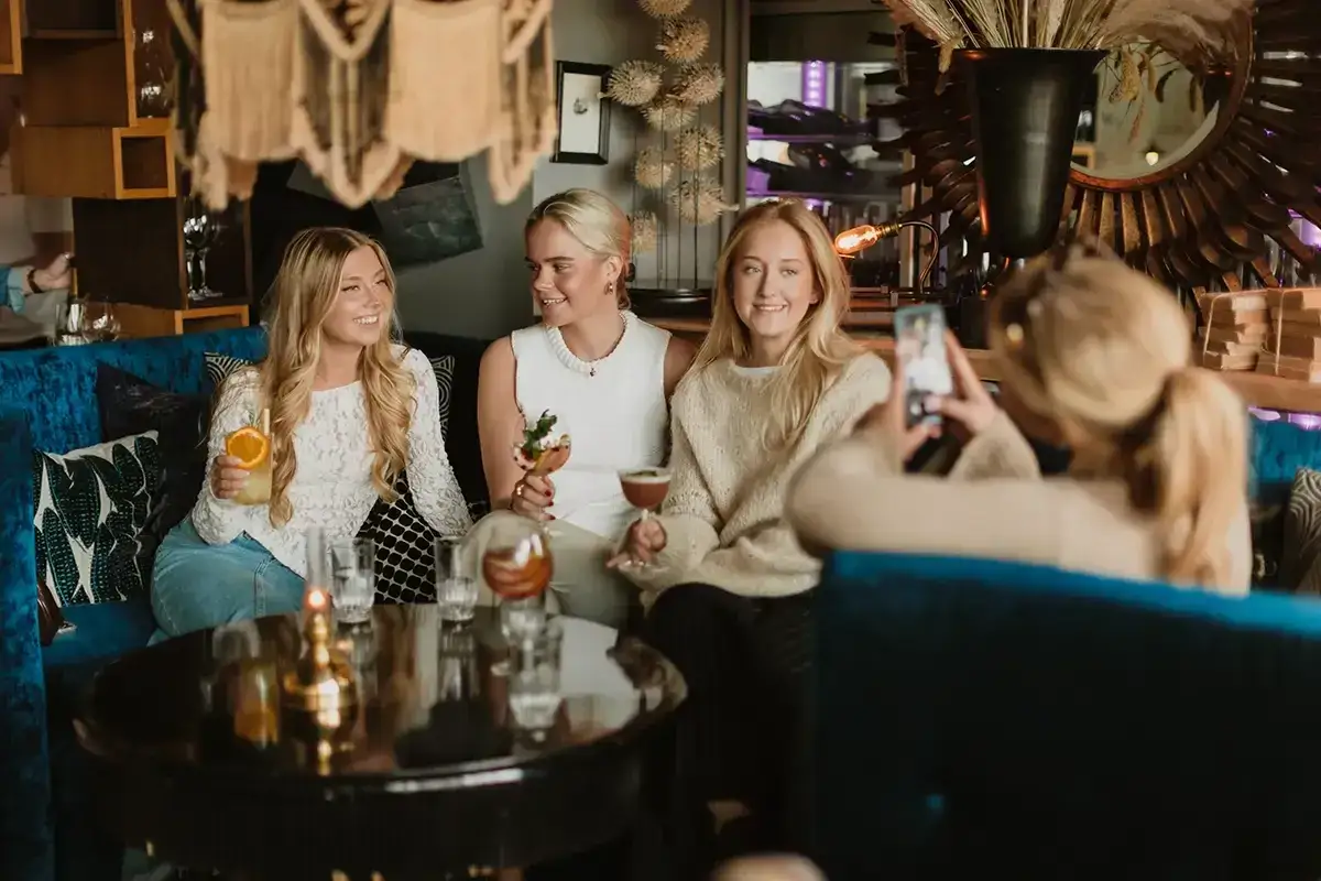Tre unga kvinnor njuter av drinkar och s&auml;llskap under en mysig griffins brunch.