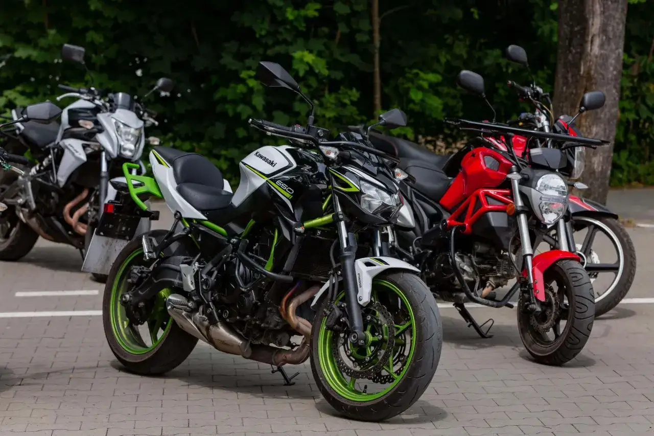 Trzy motocykle: biało-czarny Kawasaki z zielonymi akcentami (kategoria A2), czerwony i biały.