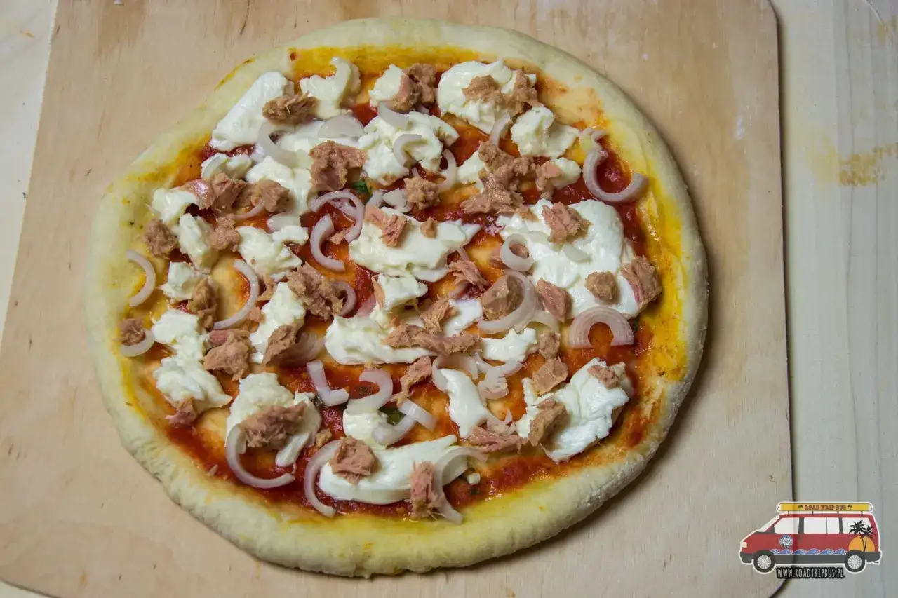 Nieupieczona pizza z tuńczykiem, mozzarellą i cebulą na drewnianej desce. Idealna na szybki obiad.