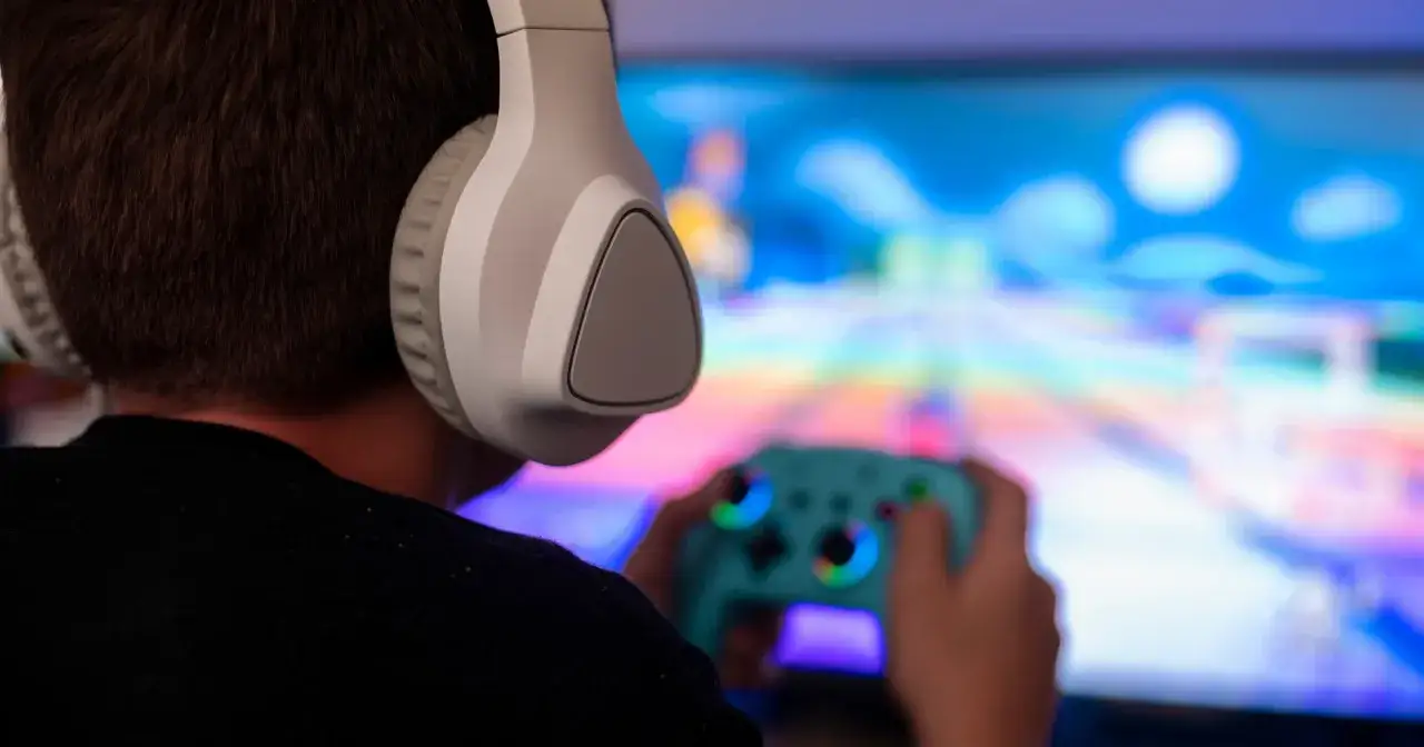 Chłopiec w słuchawkach gra na PS4. Kolorowy ekran i pad sugerują gry dla dzieci, nawet 3-latka.