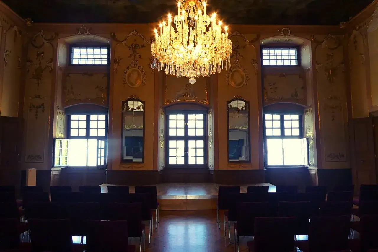 Prunkvoller Saal im Meersburg Neues Schloss mit Kronleuchter und Reihen von Stühlen, bereit für eine Veranstaltung.