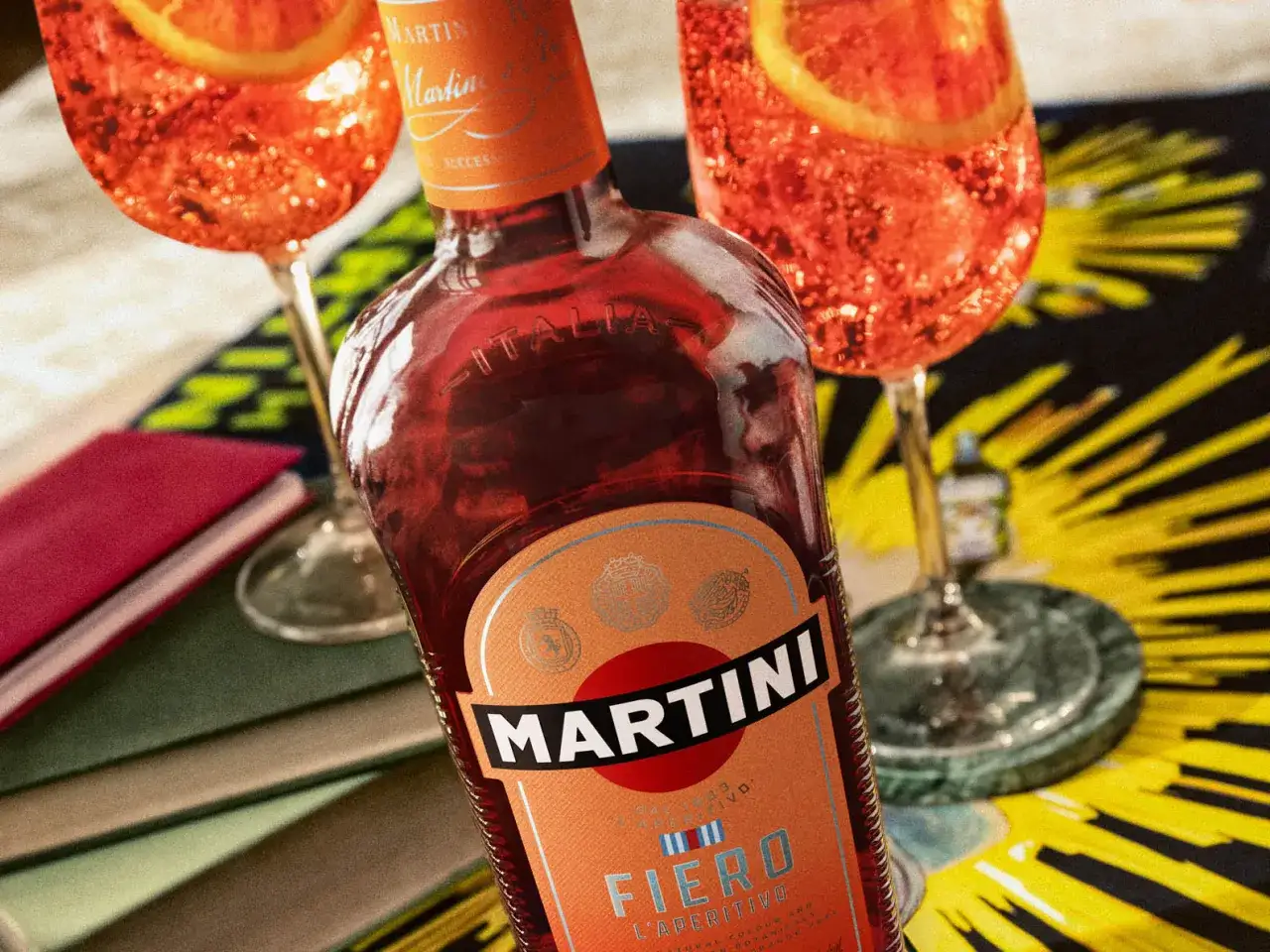 Bouteille de Martini Fiero et deux cocktails pétillants ornés de tranches d'orange, prêts pour un apéritif.