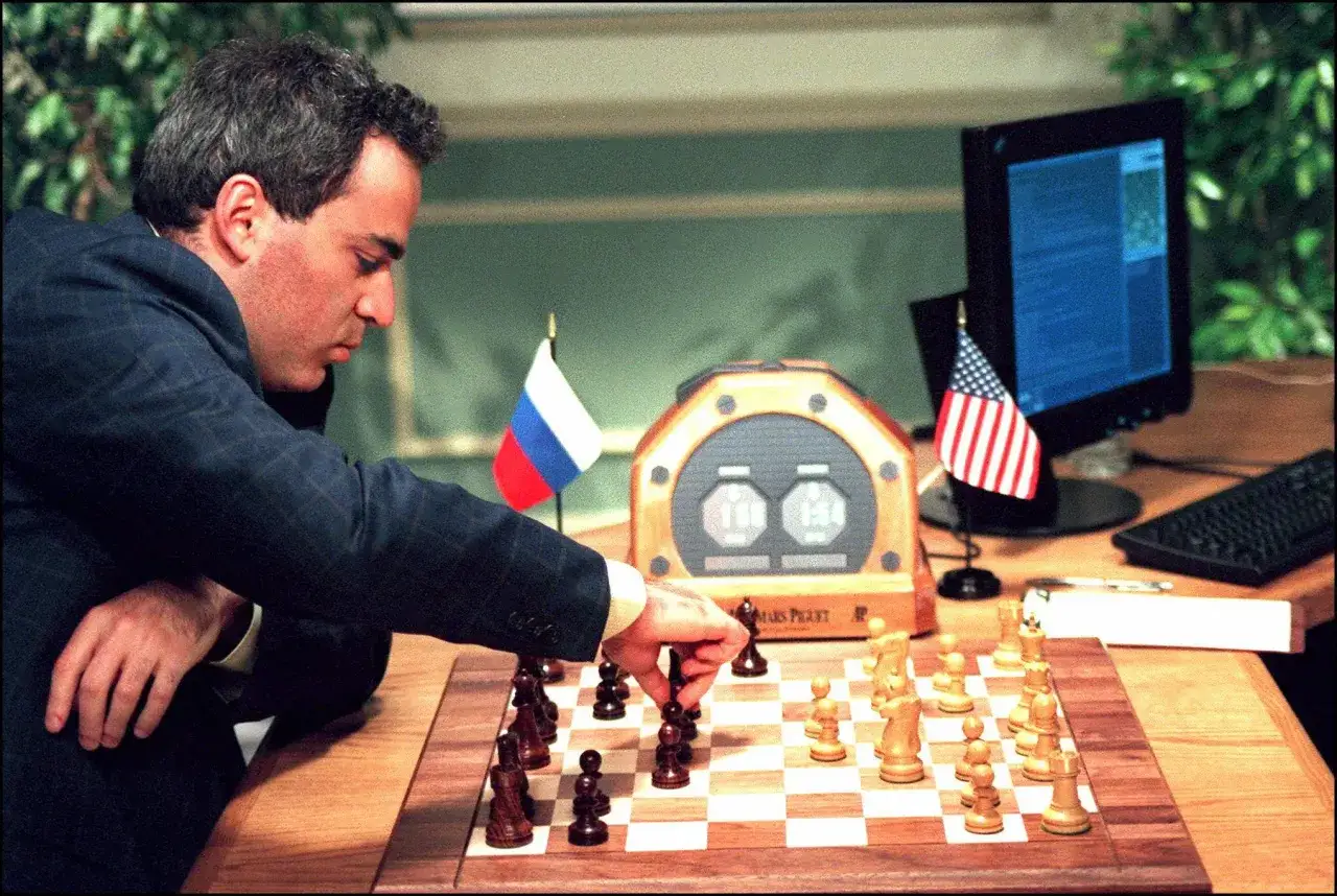 Garry Kasparov, concentré, joue aux échecs contre Deep Blue. Drapeaux russe et américain, horloge d'échecs et ordinateur visibles.