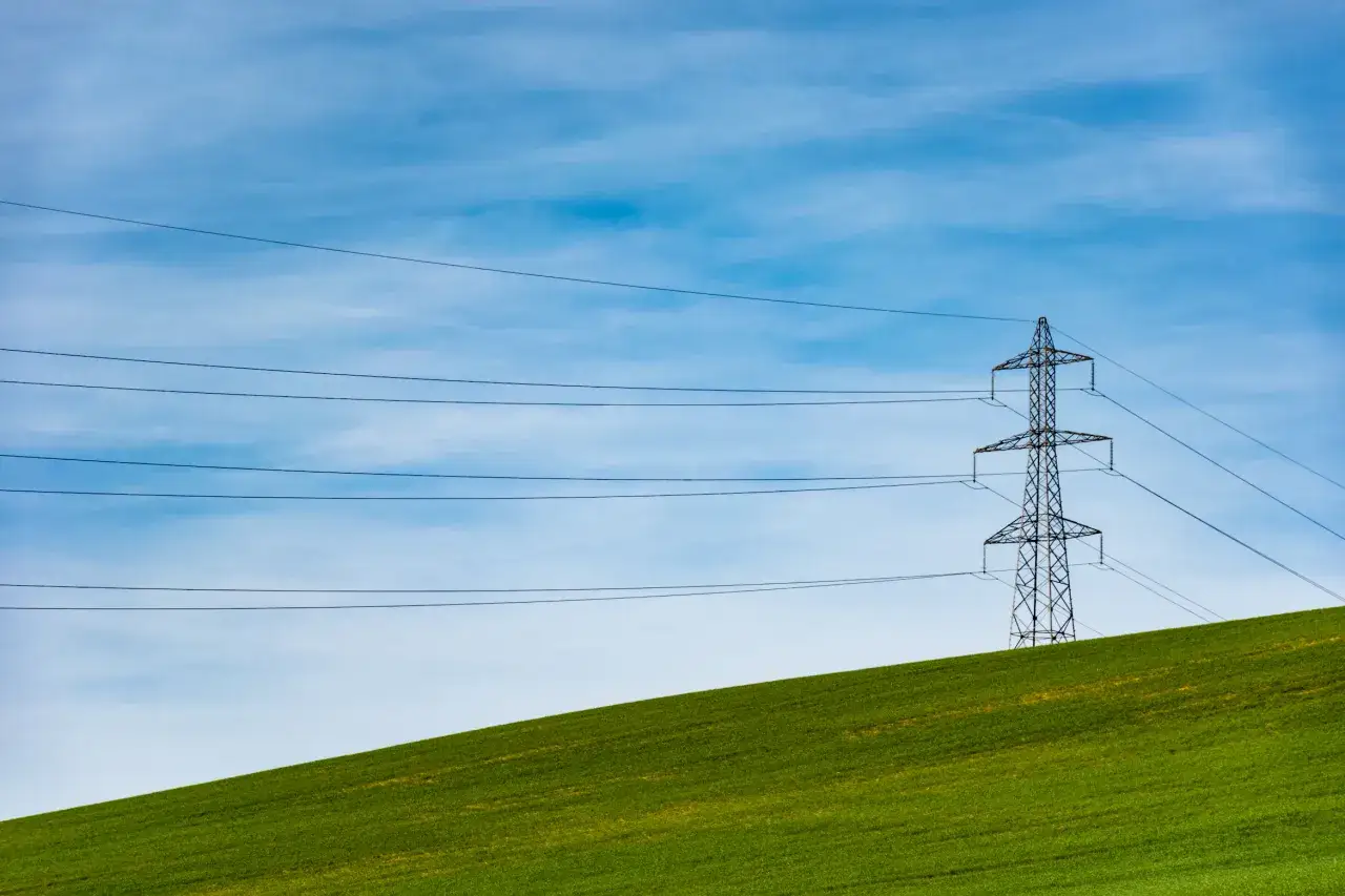 Linie energetyczne na tle błękitnego nieba, symbolizujące zmianę dostawcy prądu. Zielone pole wznosi się ku górze.
