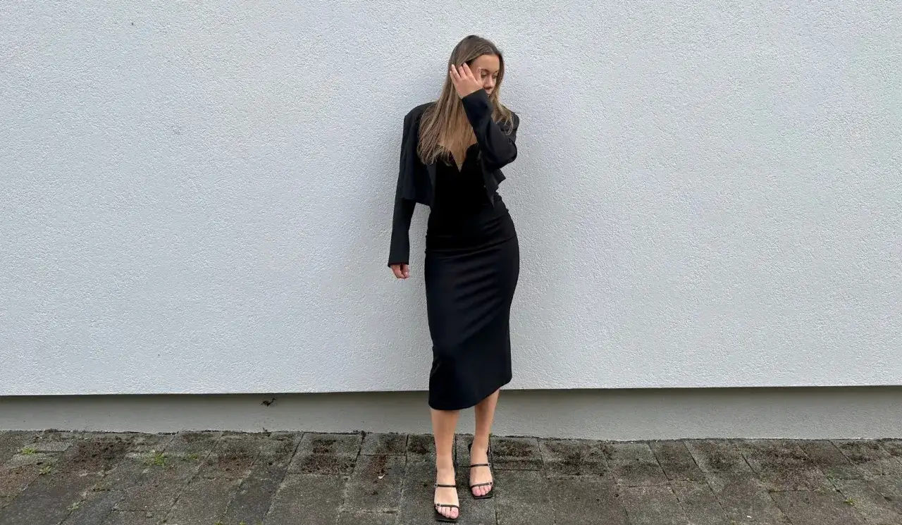Elegancka kobieta w czarnej sukience i marynarce, gotowa na wieczór w filharmonii. Jej buty na obcasie dodają szyku.