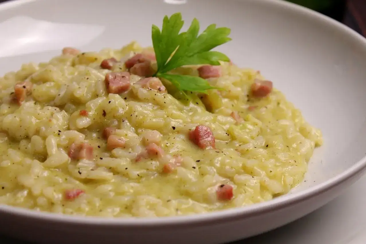 Risotto cremoso con zucchine e cubetti di pancetta croccante, guarnito con prezzemolo fresco.