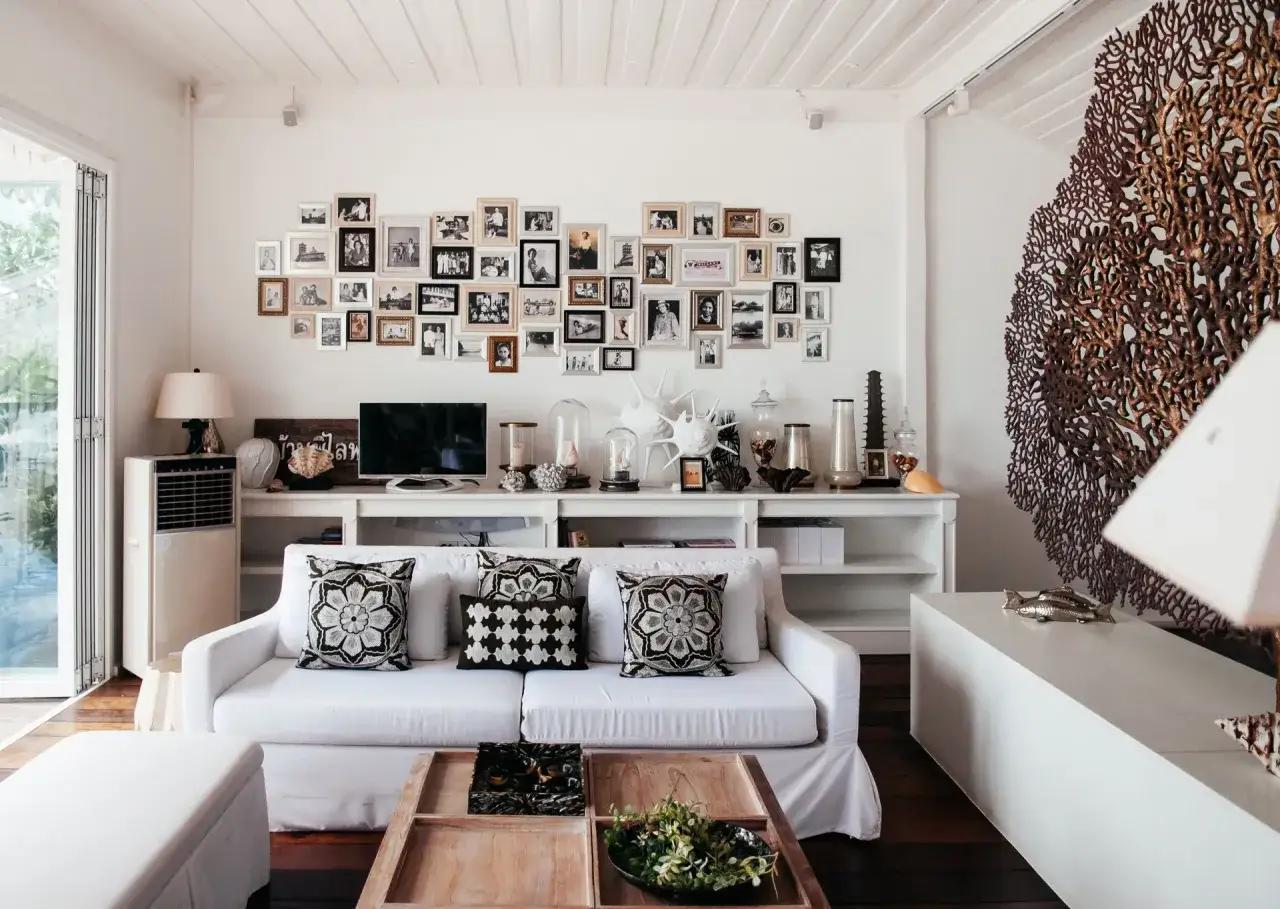 Sofá blanco con cojines decorativos, mesa de centro de madera y pared adornada con fotos. Una **reforma sin obras** que transforma el espacio con estilo.