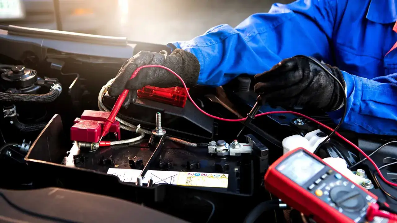 Mechaniker prüft mit Multimeter die Autobatterie. Mögliche Ursache: lichtmaschine defekt oder batterie leer.