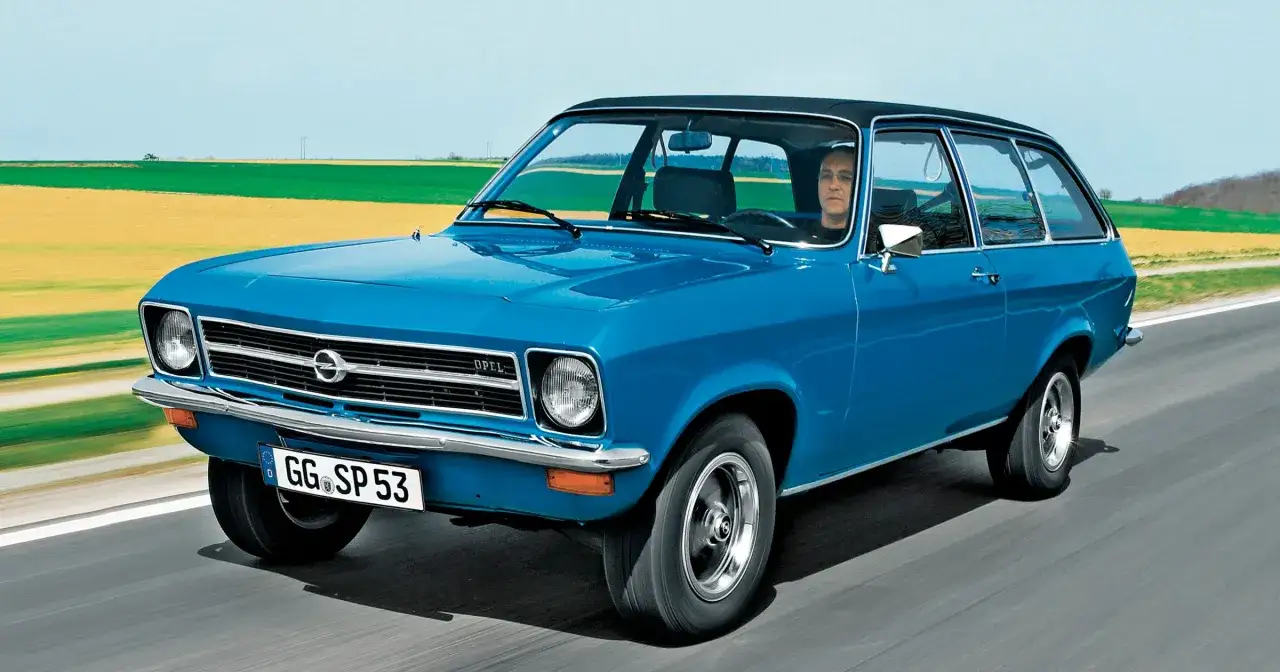 Niebieski Opel Ascona w wersji kombi jedzie po drodze, za nim pola i niebo.