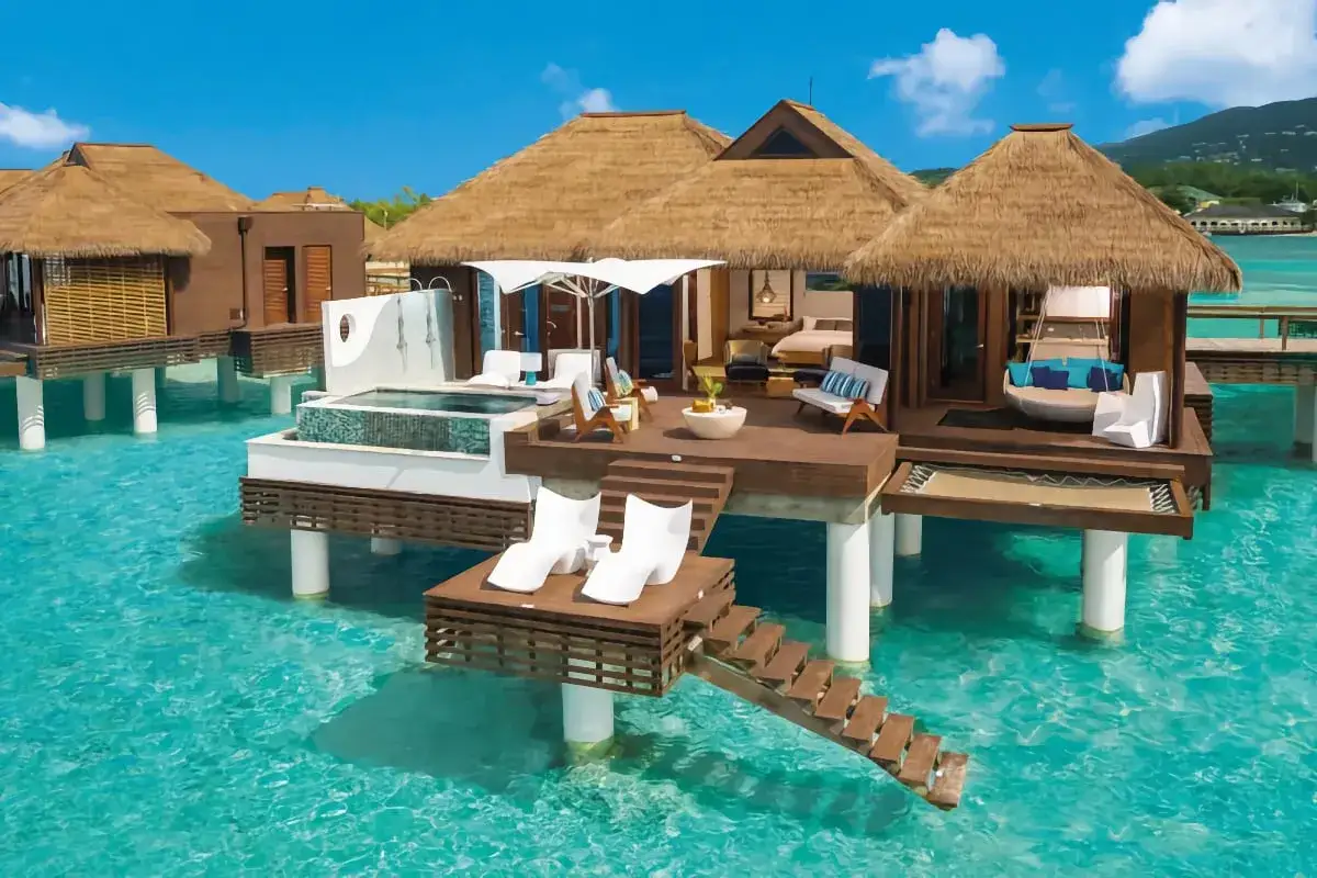 Lyxiga bungalows på styltor i turkost vatten, som en dröm på White Lotus Hotel. Solstolar och privat pool.