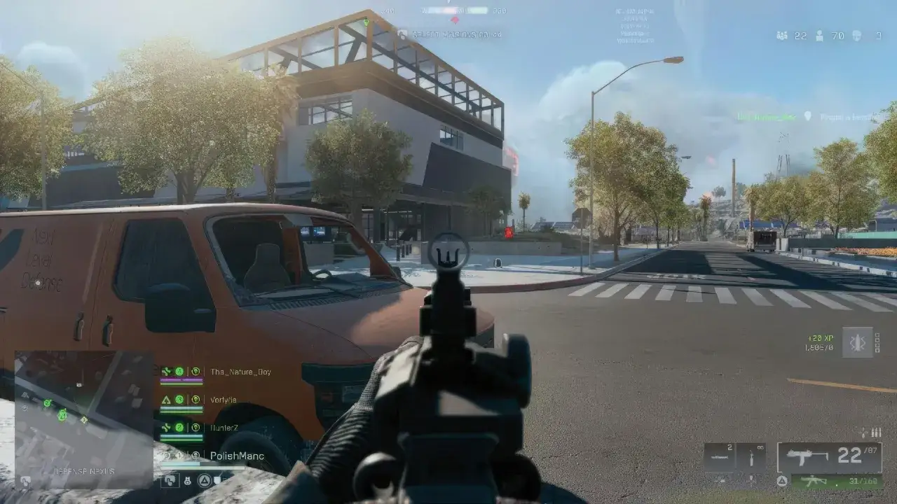 Gracz celuje z broni w grze typu battlefield battle royale. Pomarańczowy van i budynek w tle.