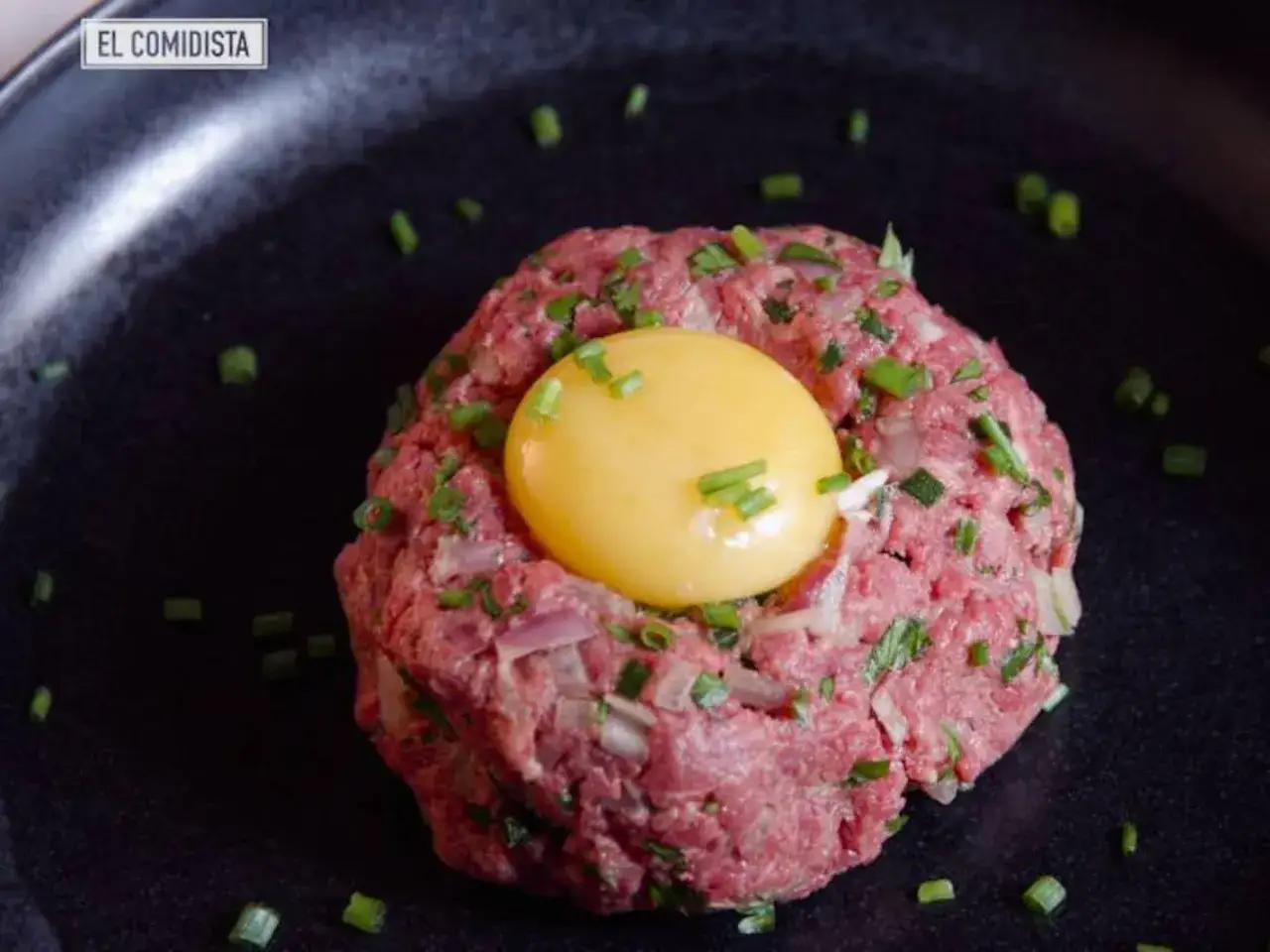 Delicioso steak tartar de wagyu con yema de huevo y cebollino picado, listo para ser mezclado.