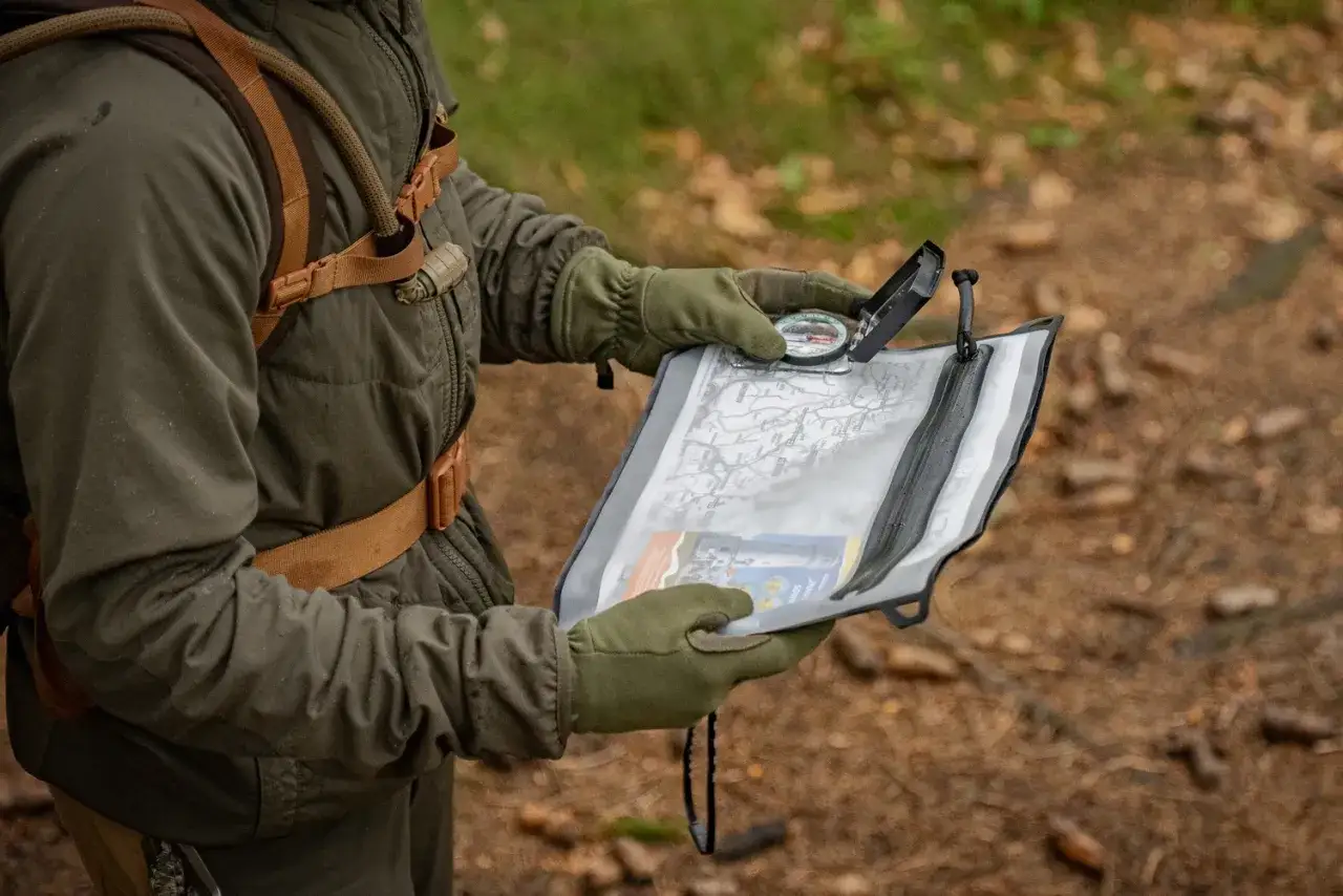Osoba w rękawiczkach sprawdza mapę i kompas, dbając o bezpieczeństwo w g&oacute;rach.