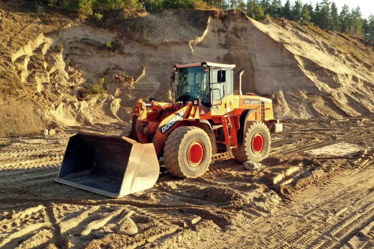 Pomarańczowa ładowarka kołowa Doosan DL300 na piaskowym placu budowy. Idealna do zdobywania klas uprawnień na koparki.
