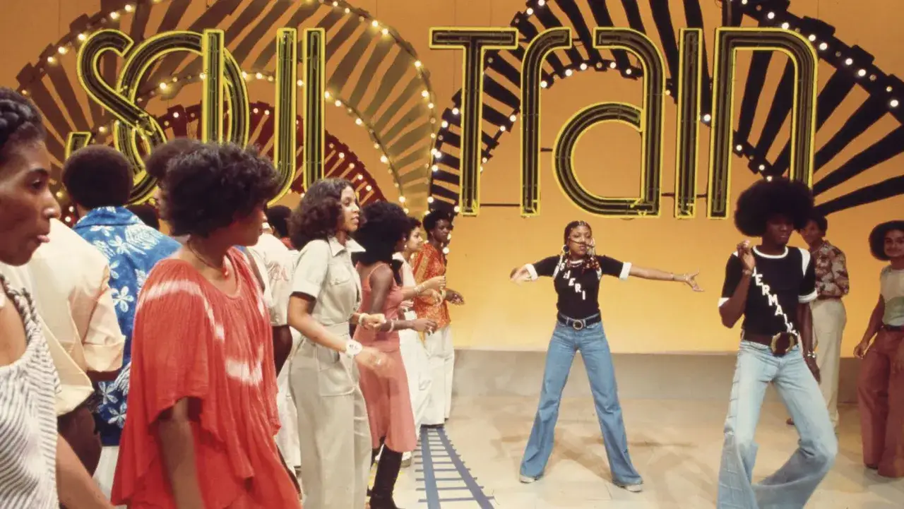 Giovani ballano al ritmo di **Soul Train**, con il logo luminoso sullo sfondo.
