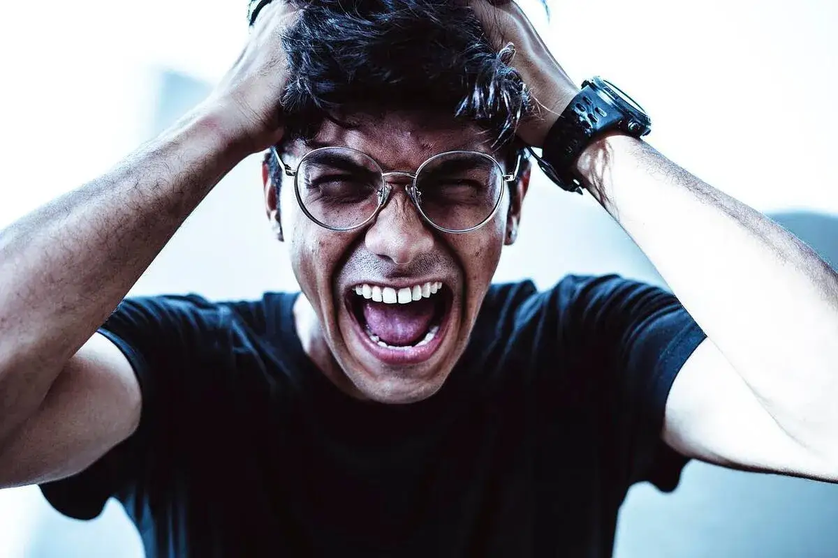 Hombre con gafas grita y se agarra la cabeza, mostrando frustración. Un ejemplo de cómo controlar la ira.