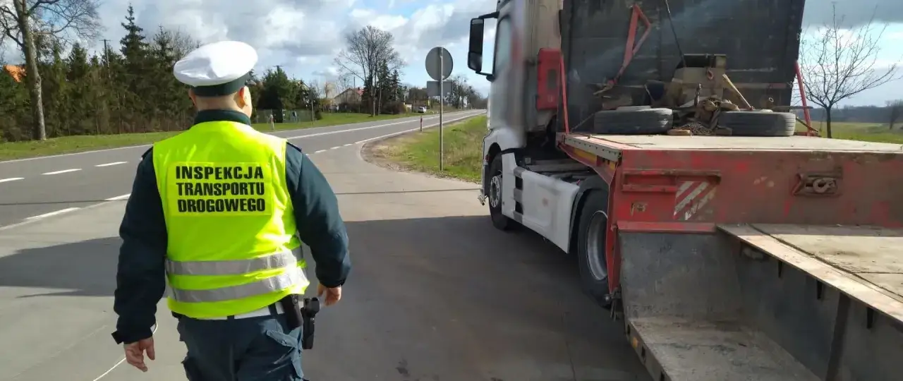 Inspektor transportu drogowego w kamizelce odblaskowej prowadzi kontrolę ciężarówki na drodze.