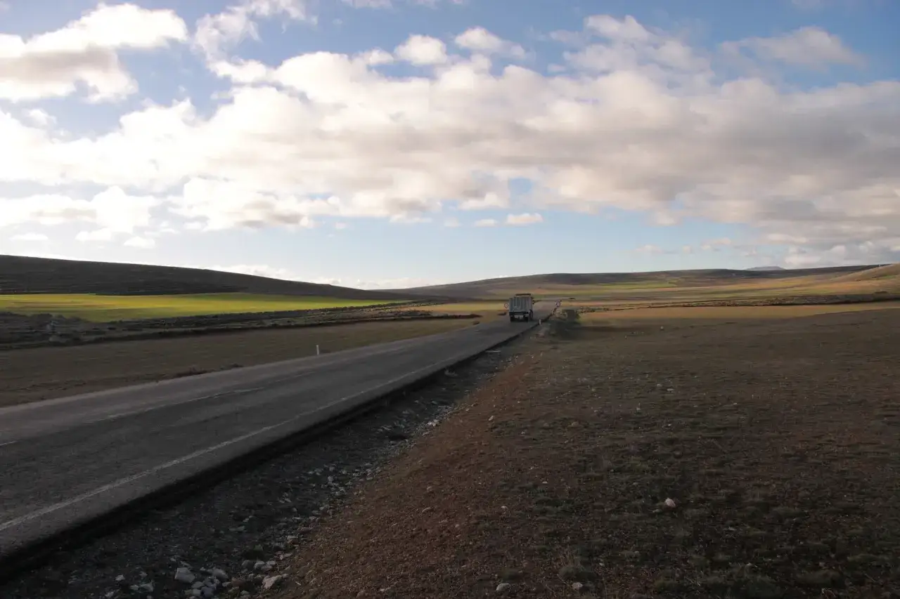 Camino solitario en Teruel, ideal para rutas por Teruel en coche. Un camión avanza por la carretera entre campos verdes y marrones bajo un cielo nublado.