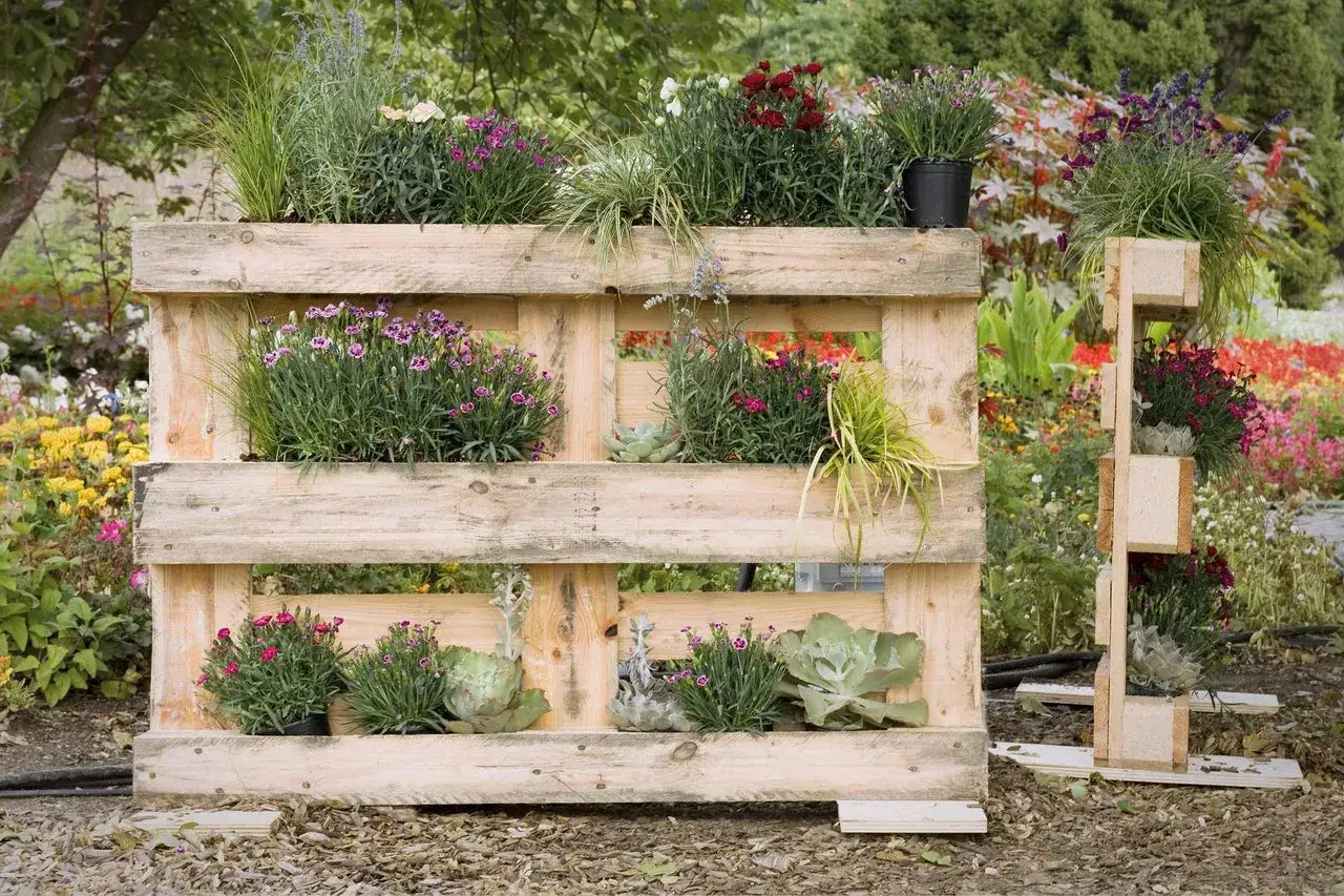 Ein schmales Hochbeet aus Paletten, bepflanzt mit bunten Blumen und Gr&auml;sern, steht im Garten.