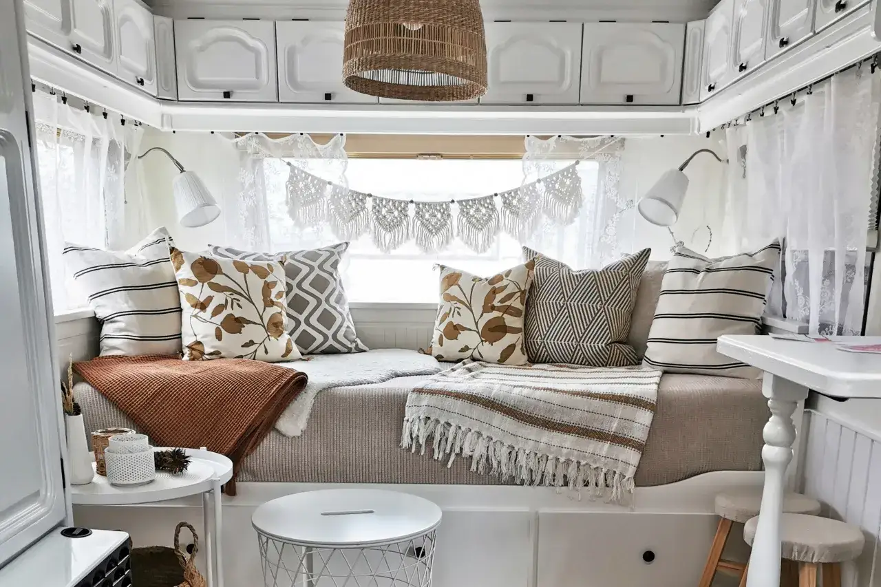 Gemütliche Wohnwagen Gardinen Ideen: Weiße Spitzenvorhänge und Makramee-Girlande schaffen Boho-Flair. Kissen und Decken laden zum Entspannen ein.