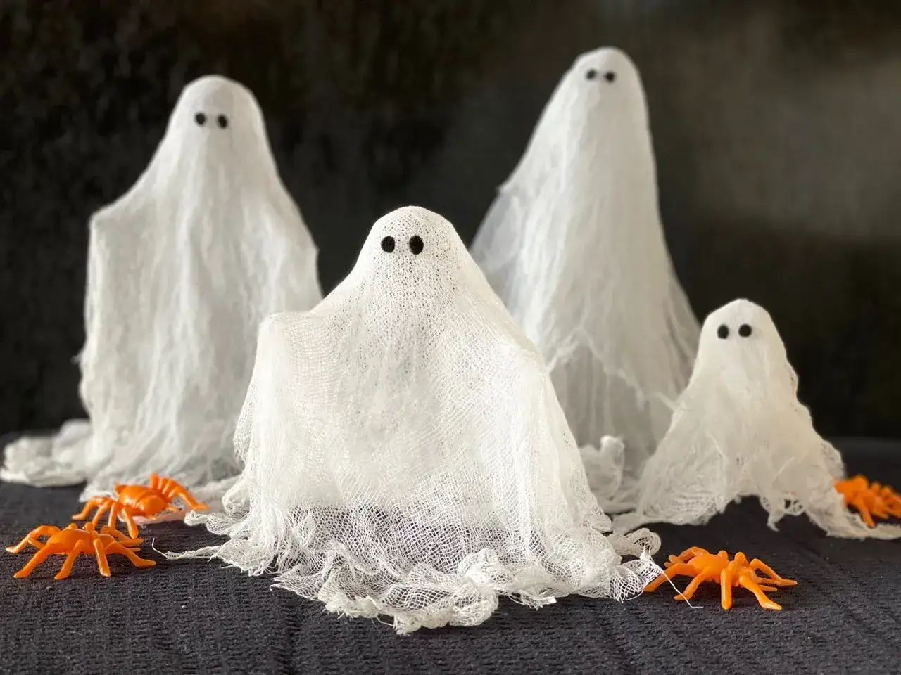 Niedliche Geister für Halloween basteln! Vier weiße Stoffgeister mit schwarzen Augen und orangefarbene Spinnen tummeln sich.