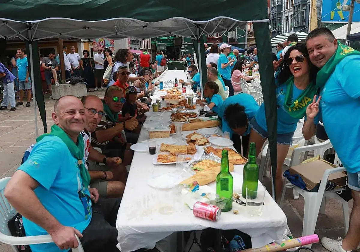 Gente disfrutando de un banquete al aire libre durante el festival de la sidra Nava. Mesas llenas de comida y bebida, ambiente festivo.