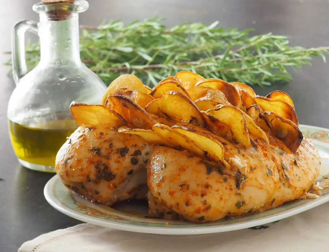 Pollo al forno con patate dorate, condito con erbe aromatiche e servito con olio d'oliva e rosmarino fresco.