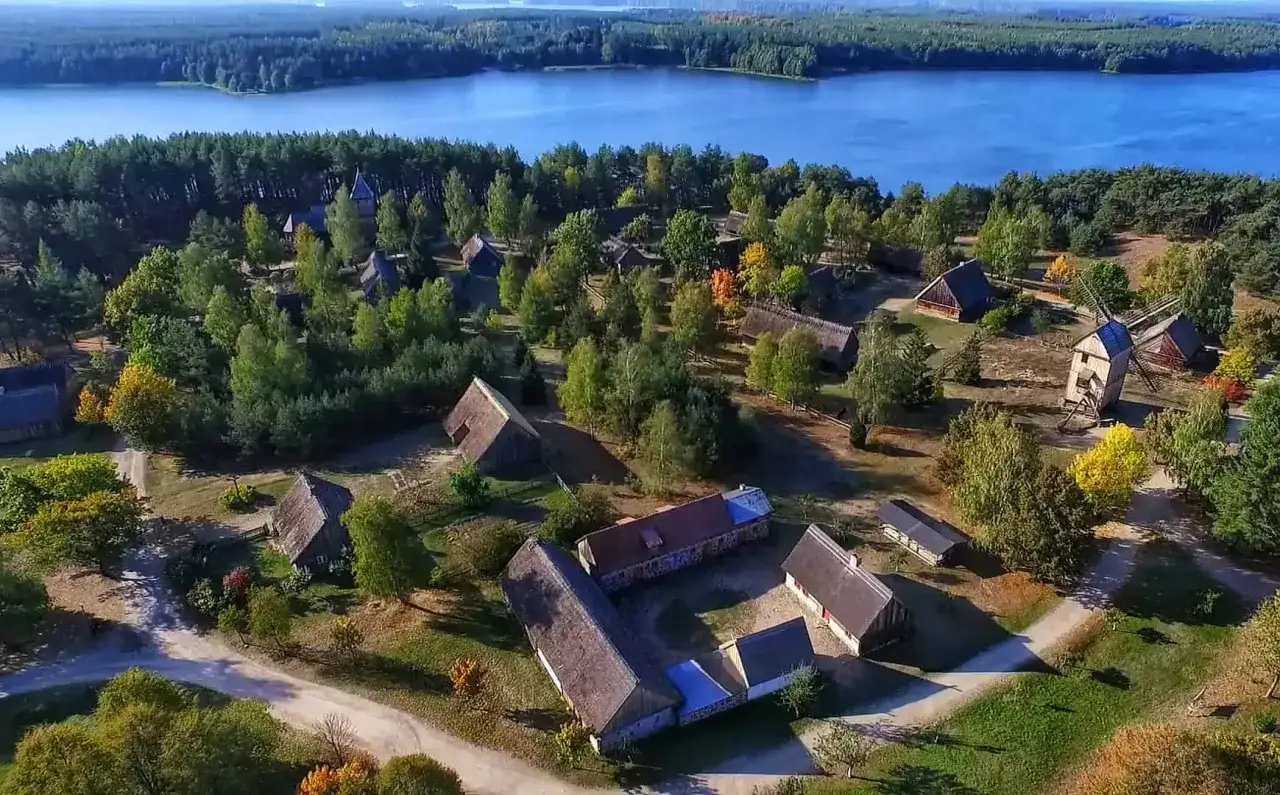 Skansen nad jeziorem, gdzie słychać echo kaszubskiego języka. Drewniane chaty, wiatrak i las tworzą malowniczy krajobraz.