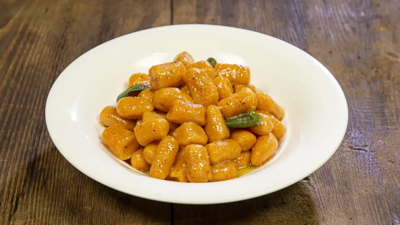 Un piatto di gnocchi di zucca dorati, conditi con burro fuso e salvia, su un tavolo di legno rustico.