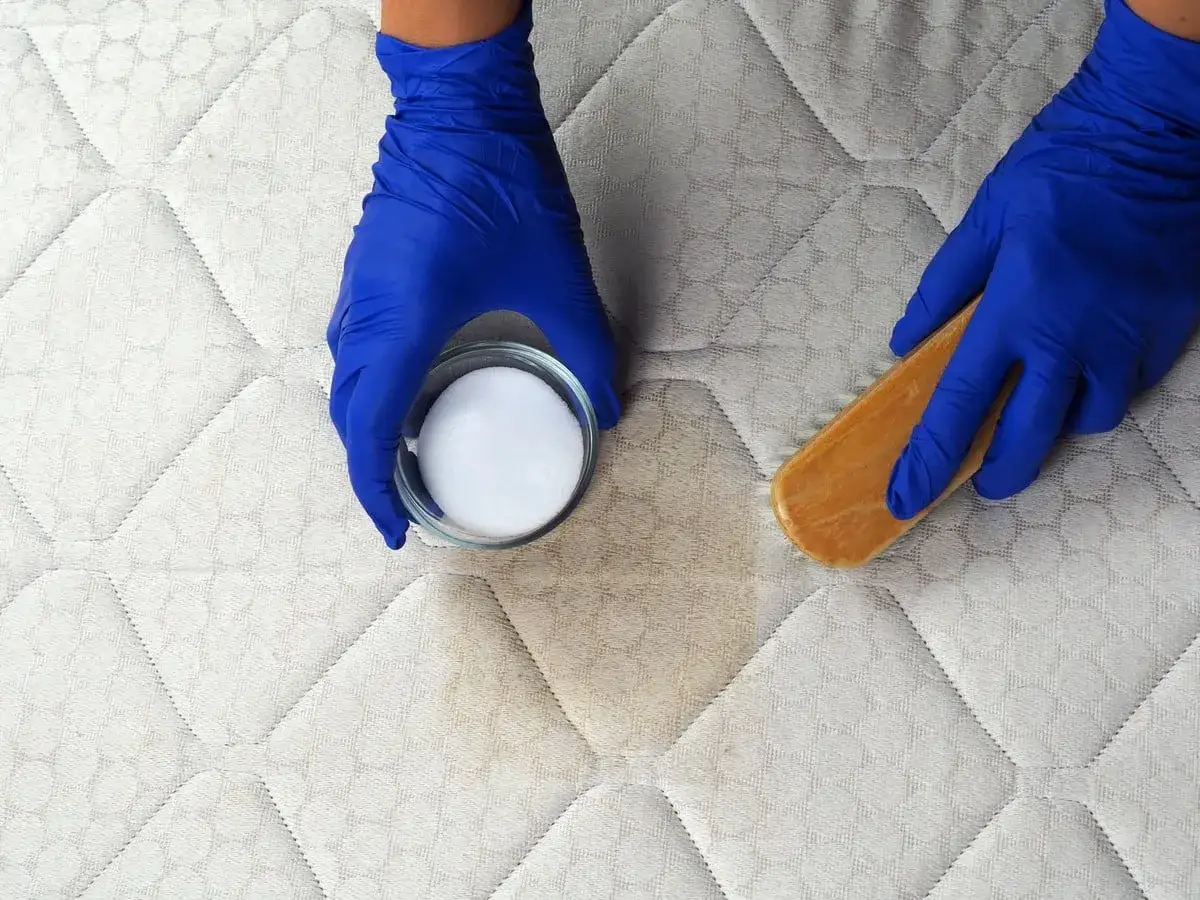 Mains gantées appliquant de l'eau oxygénée sur une tache de sang sur un matelas.