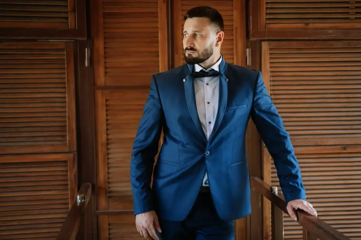 Elegancki mężczyzna w granatowym garniturze i muszce. Idealna stylizacja, jak ubrać się na wesele mężczyzna.