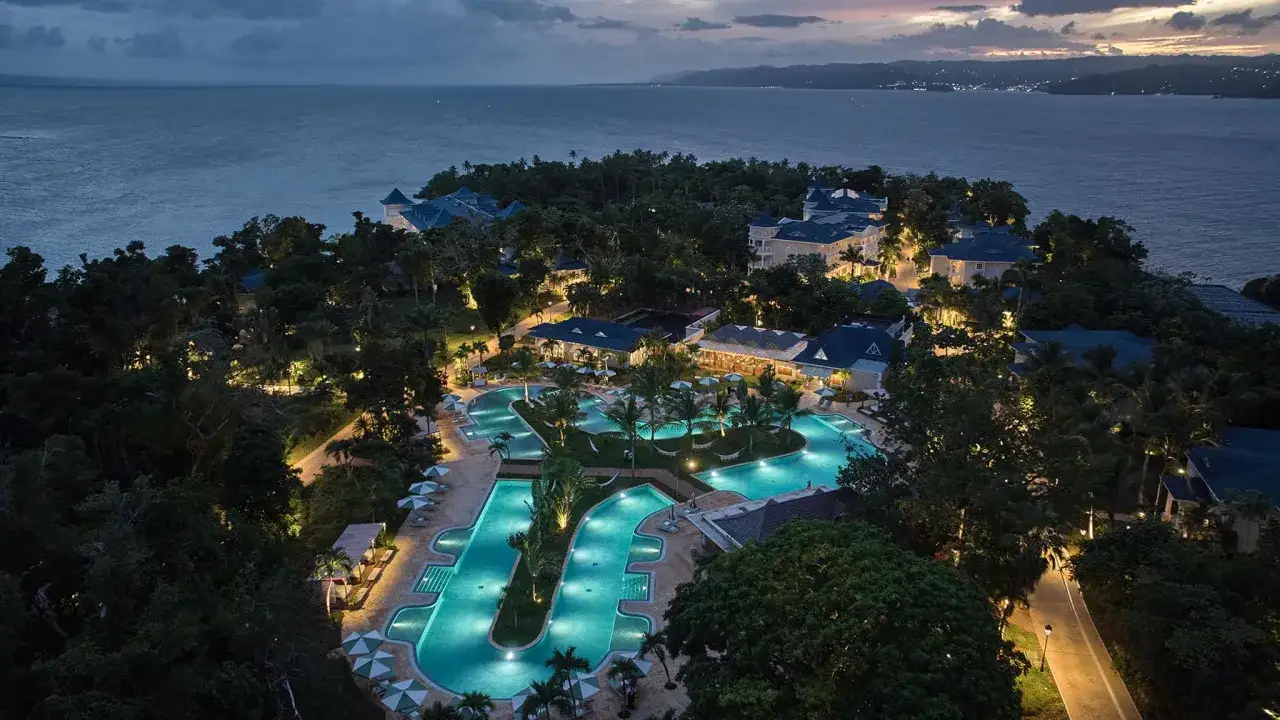 Traumhafter **Dominikanische Republik Urlaub**: Ein Resort mit beleuchteten Pools und tropischer Vegetation am Meer bei D&auml;mmerung.