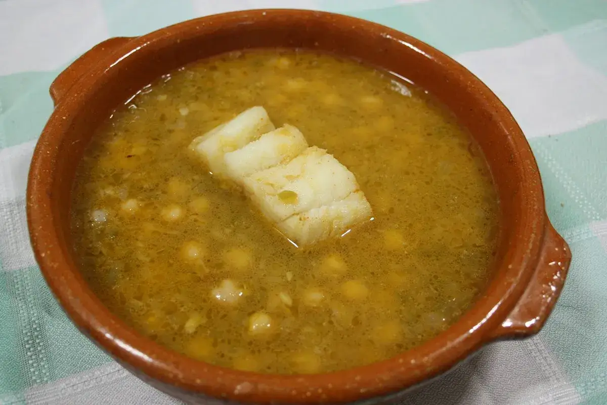 Un reconfortante plato de garbanzos con verduras y trozos de pescado blanco en una cazuela de barro.