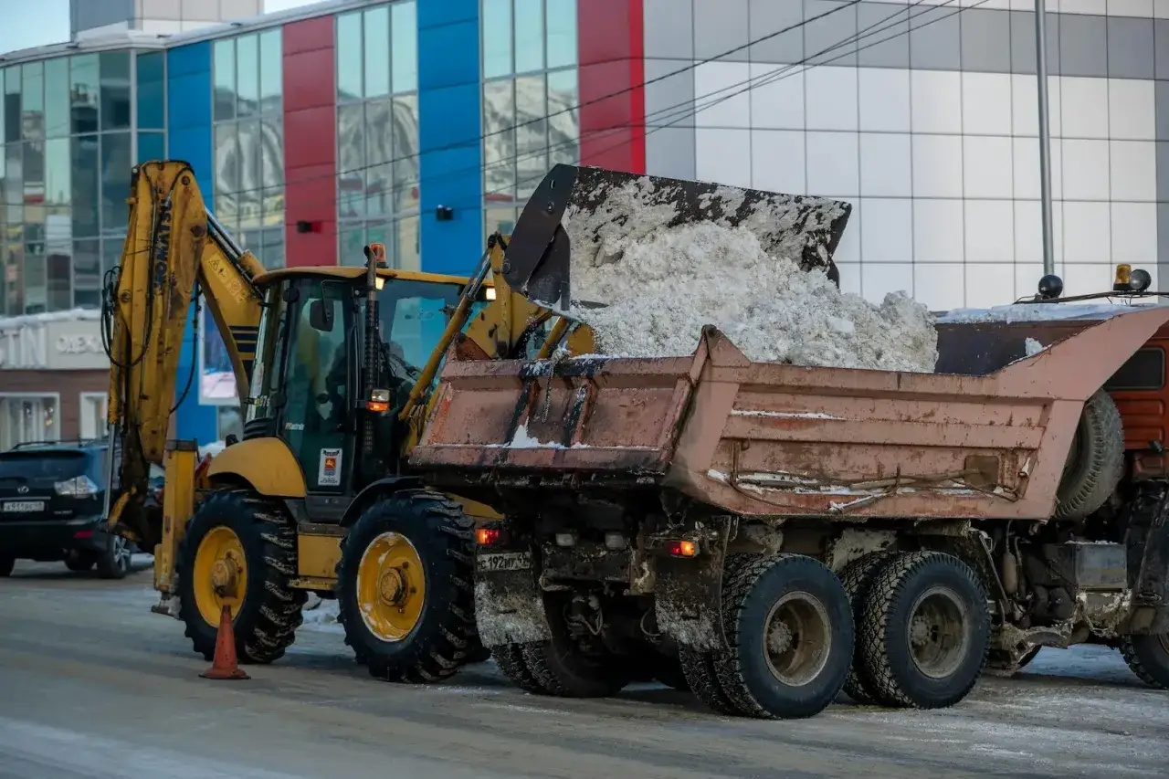 Żółta koparka kołowa Komatsu z wielką łyżką zasypuje śniegiem wywrotkę.