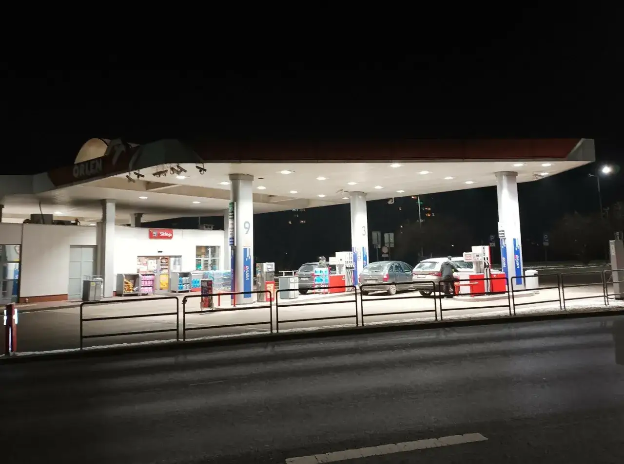 Nocna stacja Orlen. Samochody tankują, w tle widać sklep. Dostępna jest benzyna E10.