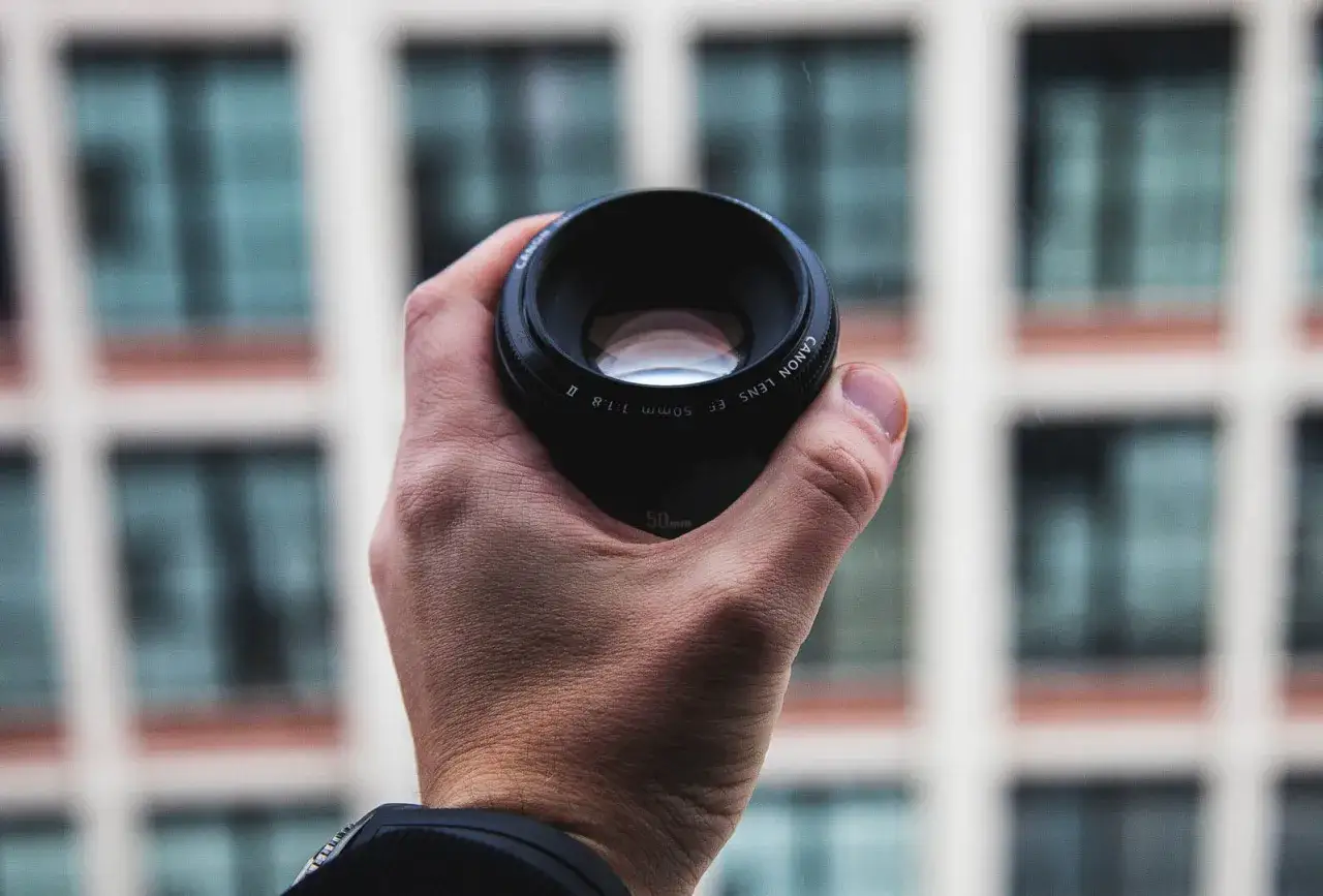 Une main tient un objectif Canon EF 50mm f/1.8 II. Cet objectif 50 mm pour quel usage ? Idéal pour les portraits et la photographie de rue.
