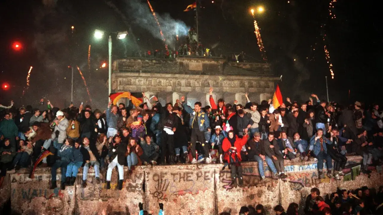 Feiernde Menschen auf der Berliner Mauer mit Feuerwerk. Eine lebendige Zusammenfassung der Wiedervereinigung Deutschlands.